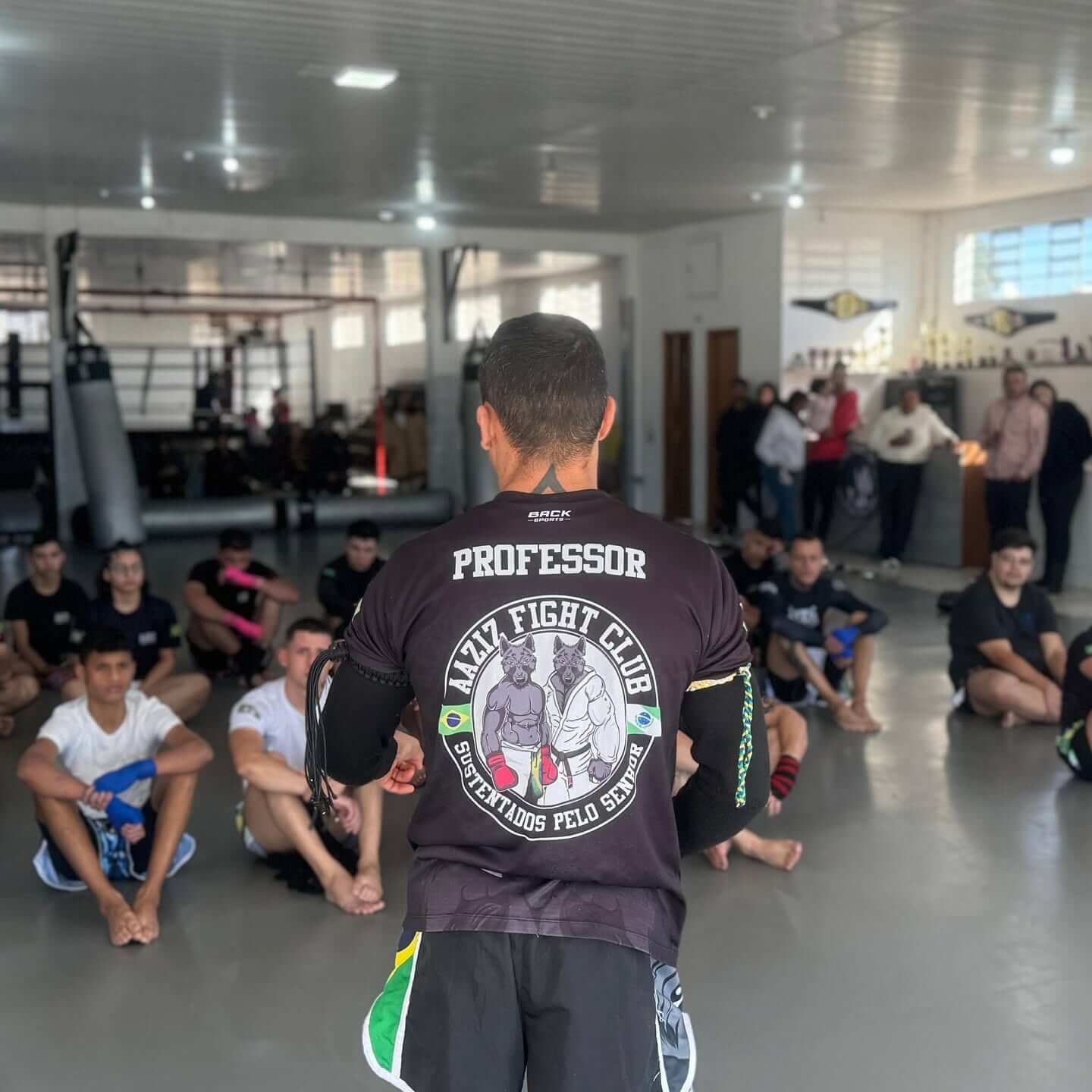 Professor da AAZIZ Fight Club conduzindo a aula com os alunos sentados no tatame